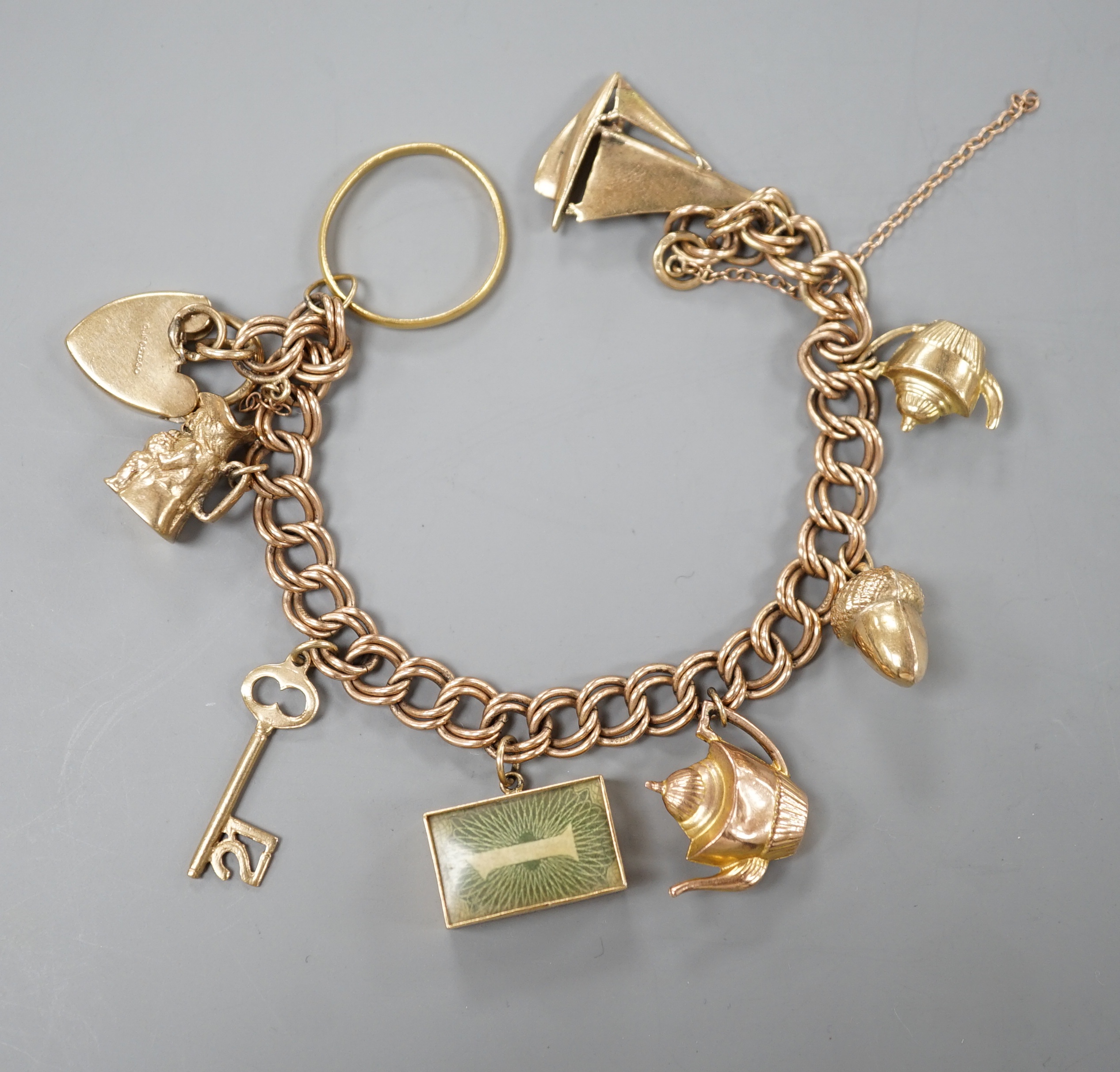 A 1960's 9ct gold charm bracelet, hung with eight assorted mainly 9ct gold charms and a 22ct gold wedding band, gross 28.4 grams.